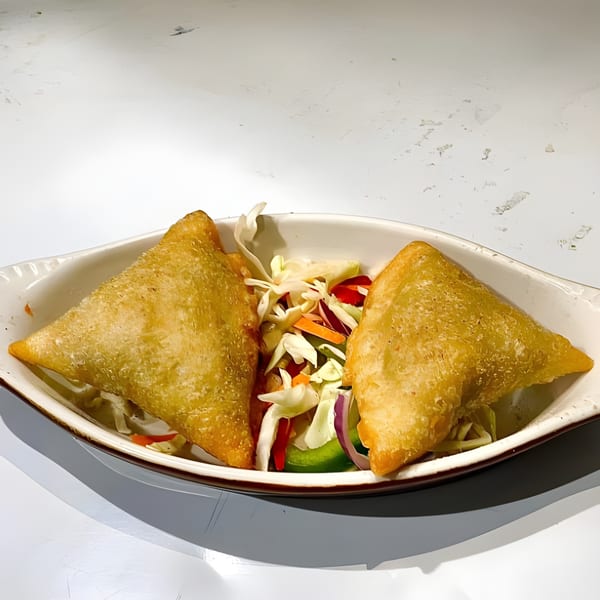 Two golden-brown samosas with a side of fresh shredded cabbage, carrots, and red onion.