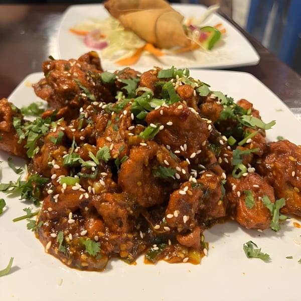 Indian chili chicken with sesame seeds and cilantro, with a spring roll in the background.