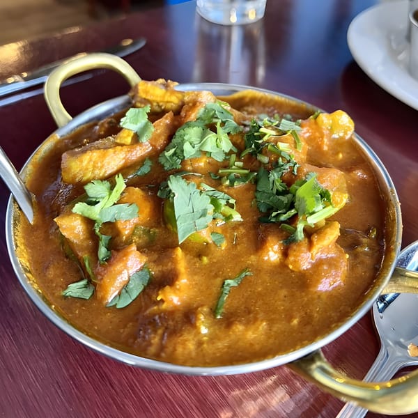 A close-up of a chicken curry dish, garnished with fresh cilantro, in a traditional Indian serving bowl.