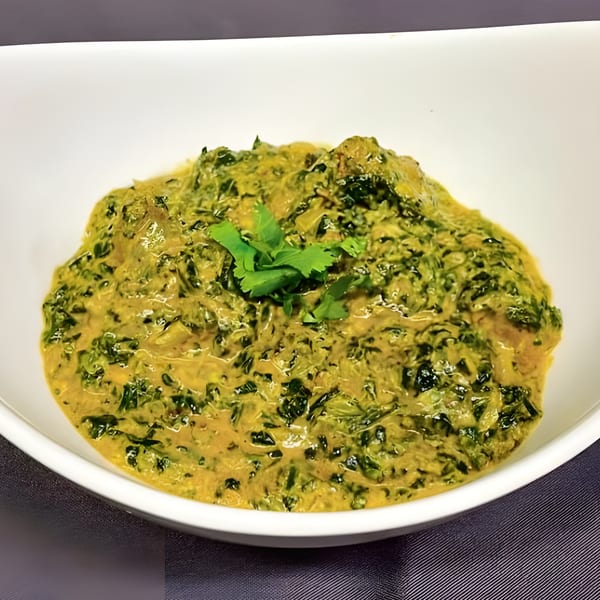 Palak Paneer, a creamy Indian spinach and cheese dish, garnished with fresh cilantro in a white bowl.